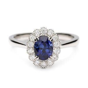 Platinum sapphire and diamond halo engagement ring featuring an oval blue sapphire with a milgrain-edged diamond cluster.