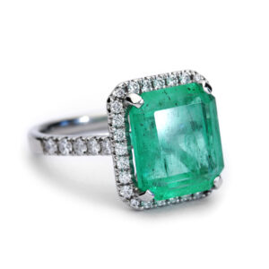 Platinum halo engagement ring with a 5.59ct rectangular re-cut emerald surrounded by round brilliant diamonds.